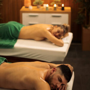 Young woman and mid adult man relaxing in spa center after massage together. Nice cozy space with candles in background make them feeling wonderful