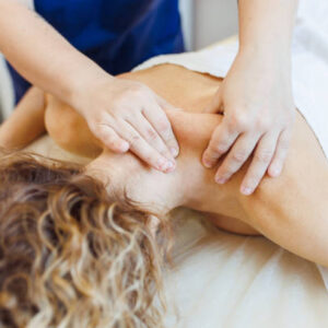 Skilled female spa therapist administers deep tissue massage, focusing on client shoulder area to alleviate stubborn muscle tension, squeezing and moving tissue. Caucasian female client with curly fair hair enjoys therapeutic benefits of professional treatment, seeking relief from discomfort