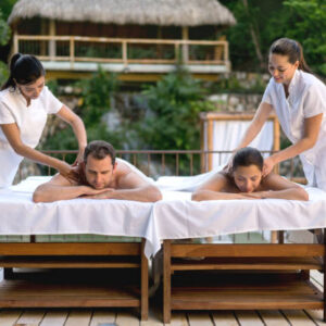 Happy couple getting a back massage outdoors at the spa by two beautiful masseuses - lifestyle concepts