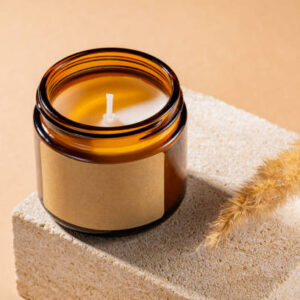 Mock-up of aroma soy candle in amber glass jar on natural stone pedestal. Scented cozy atmosphere for relax and spa on brown background, mockup